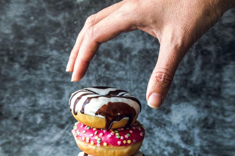 Photo of a hand reaching out to take a donut, depicting instant gratification
