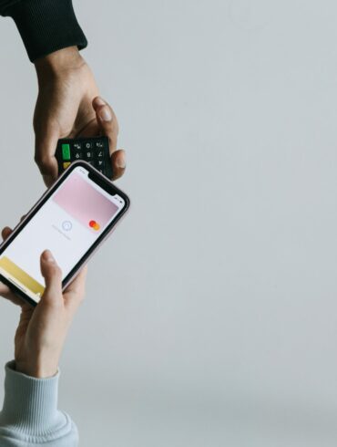 Photo of two people's hands. One using a smartphone NFC feature to make a contactless payment, while the other one holds out the payments processing machine.