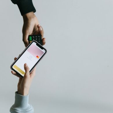 Photo of two people's hands. One using a smartphone NFC feature to make a contactless payment, while the other one holds out the payments processing machine.