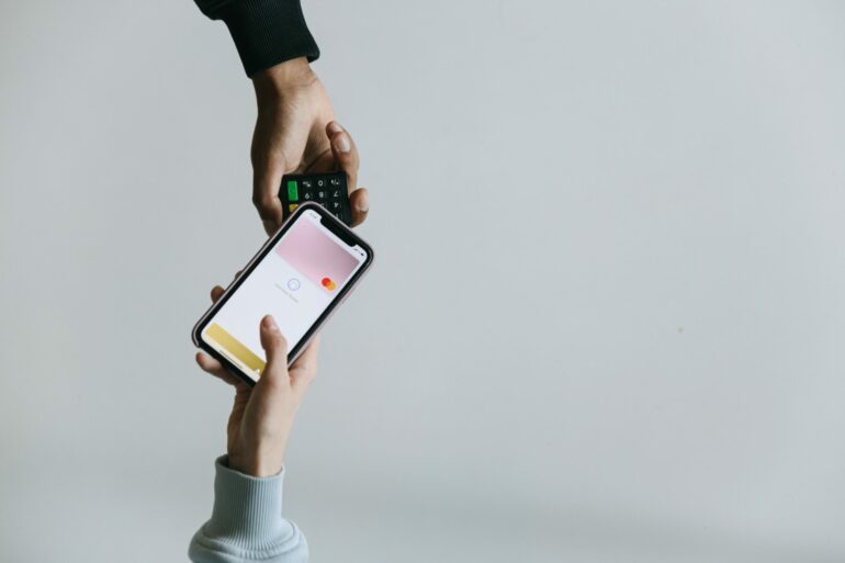 Photo of two people's hands. One using a smartphone NFC feature to make a contactless payment, while the other one holds out the payments processing machine.