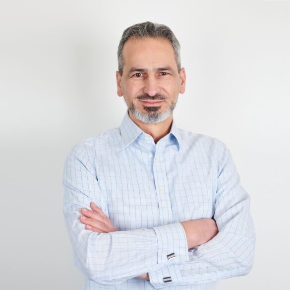 A professional business photo of Alex Mifsud as he poses wearing a light-blue chequered shirt with crossed arms