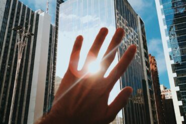 Photo of a hand blocking the sun's reflection from a big building in a city centre