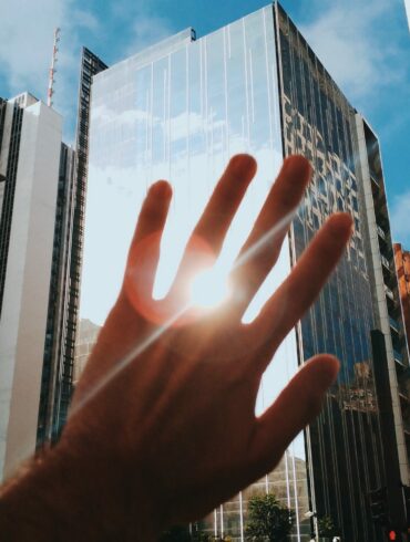 Photo of a hand blocking the sun's reflection from a big building in a city centre