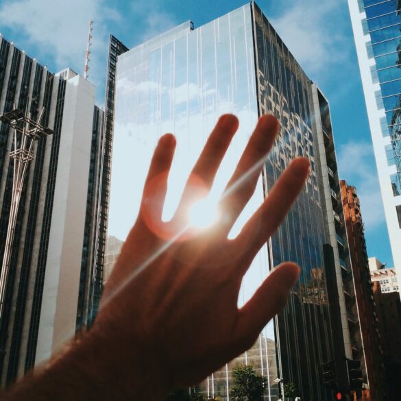 Photo of a hand blocking the sun's reflection from a big building in a city centre