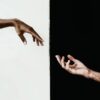 An interesting photo of an artistic style image with a white persons hand pointing towards a black persons hand.