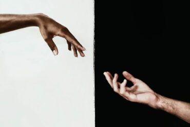 An interesting photo of an artistic style image with a white persons hand pointing towards a black persons hand.