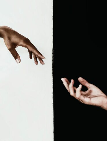 An interesting photo of an artistic style image with a white persons hand pointing towards a black persons hand.