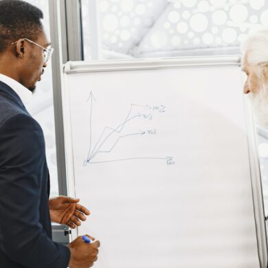 Photo of two men from diverse backgrounds in business attire making investment plans on a whiteboard with a marker