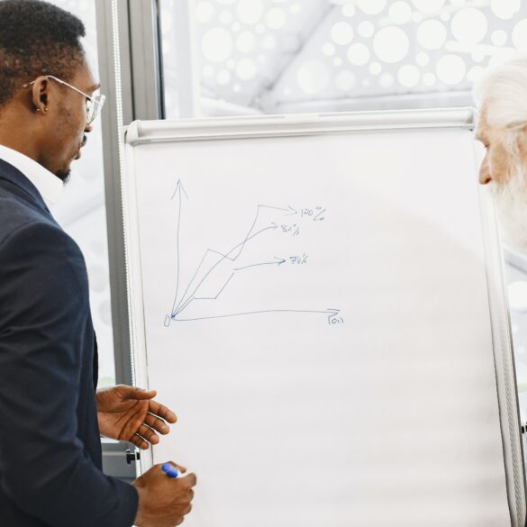 Photo of two men from diverse backgrounds in business attire making investment plans on a whiteboard with a marker