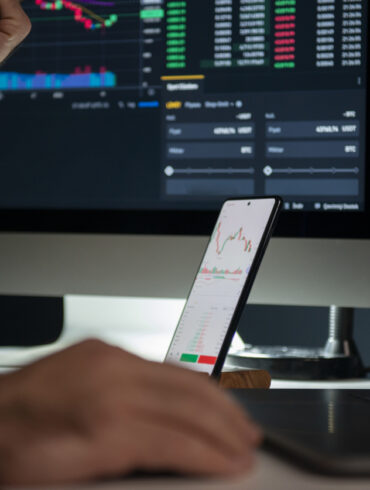 Photo of a man's hands as he trades on an exchange using both his desktop computer and smartphone at the same time.