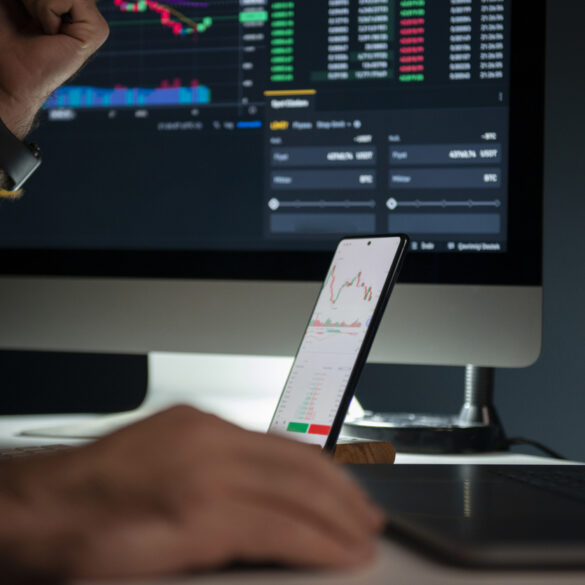 Photo of a man's hands as he trades on an exchange using both his desktop computer and smartphone at the same time.