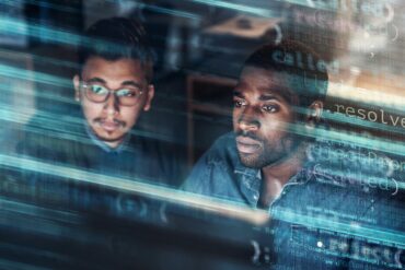 Photo of two men coding on a computer screen with an overlay over the image showing codes
