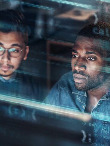 Photo of two men coding on a computer screen with an overlay over the image showing codes