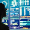 Photo of a woman in glasses looking at multiple screens with analytical data
