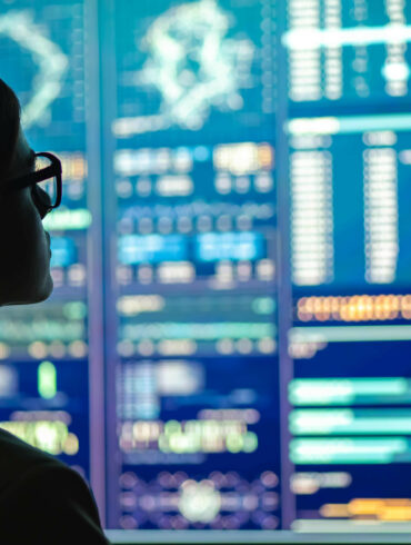 Photo of a woman in glasses looking at multiple screens with analytical data