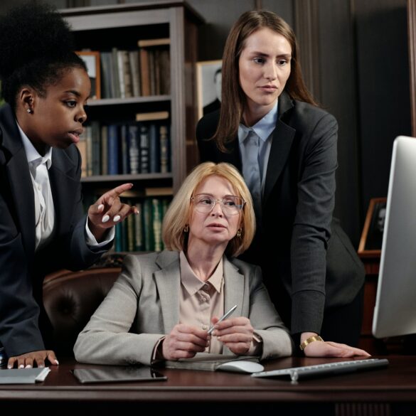 Diverse group of three women lawyers sitting around a desk in an office and making a decision together in front of a laptop.