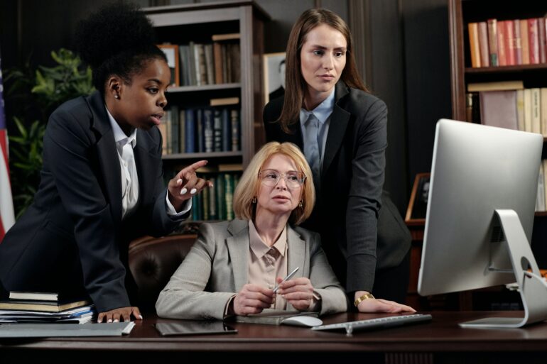 Diverse group of three women lawyers sitting around a desk in an office and making a decision together in front of a laptop.