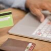 Photo of a woman's hand holding a credit card as she makes a payment on her laptop