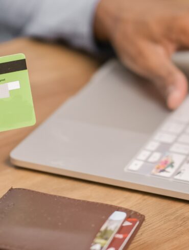 Photo of a woman's hand holding a credit card as she makes a payment on her laptop