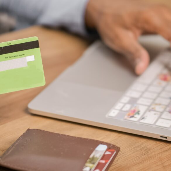 Photo of a woman's hand holding a credit card as she makes a payment on her laptop