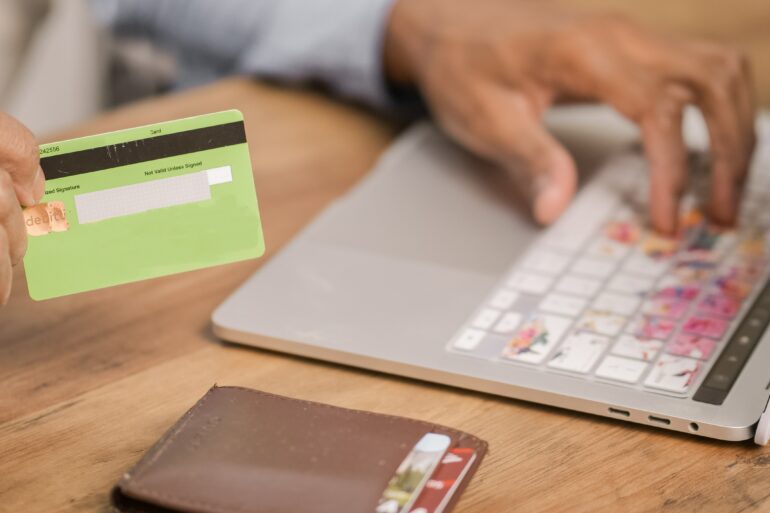 Photo of a woman's hand holding a credit card as she makes a payment on her laptop
