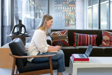 Photo of a woman using a laptop on her coffee table to make a conference call while working from home