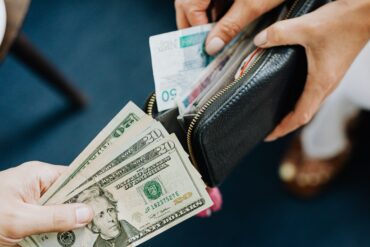 Photo of two people opening their wallets to trade foreign currencies. One person offers dollars while the other offers a foreign note in exchange.