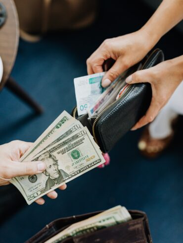 Photo of two people opening their wallets to trade foreign currencies. One person offers dollars while the other offers a foreign note in exchange.