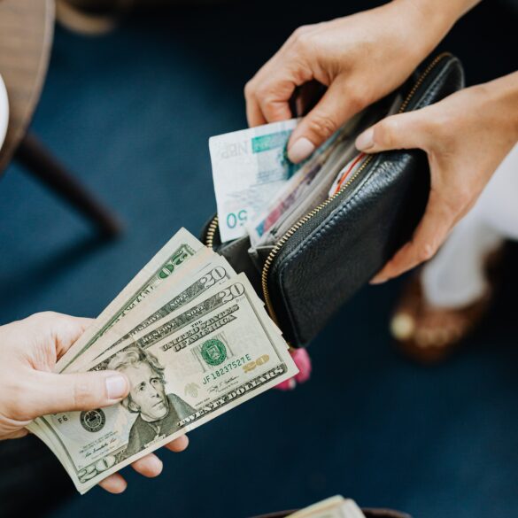 Photo of two people opening their wallets to trade foreign currencies. One person offers dollars while the other offers a foreign note in exchange.