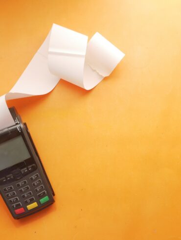 Photo of an empty invoice being printed out of a card reader on a surface with an orange background