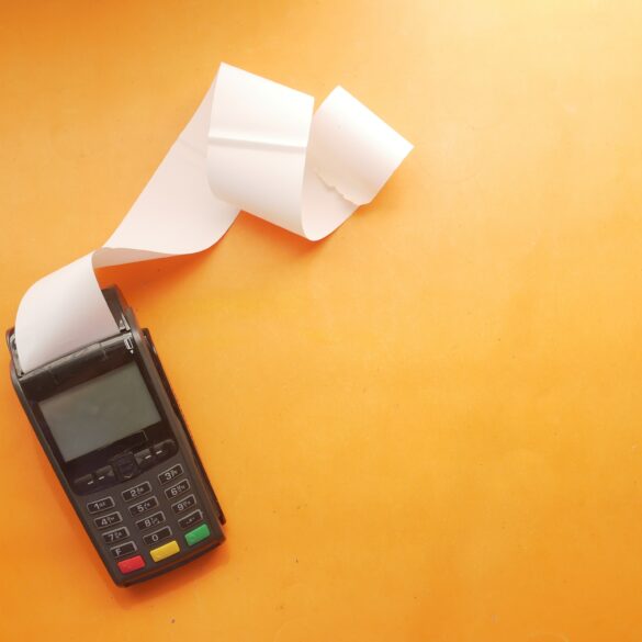 Photo of an empty invoice being printed out of a card reader on a surface with an orange background