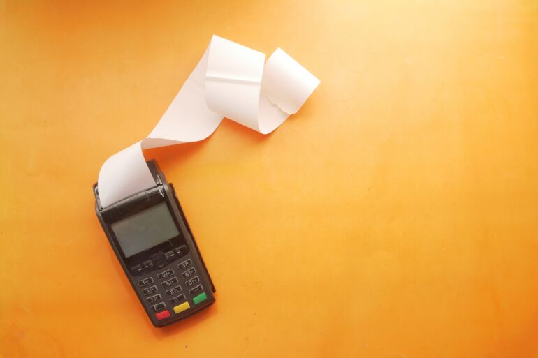 Photo of an empty invoice being printed out of a card reader on a surface with an orange background