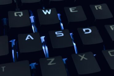 A close-up photo of a backlit qwerty keyboard in the dark