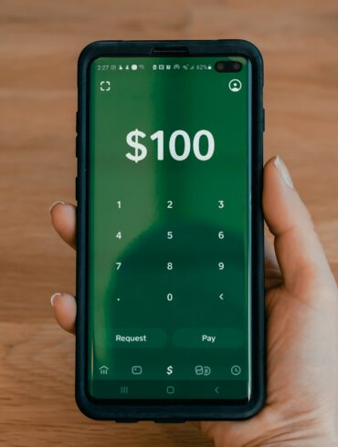 Photo of a woman's hand as she makes a payment transfer of $100 on her smartphone