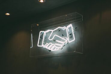Photo of hand-shake neon lights flashing on the wall at night