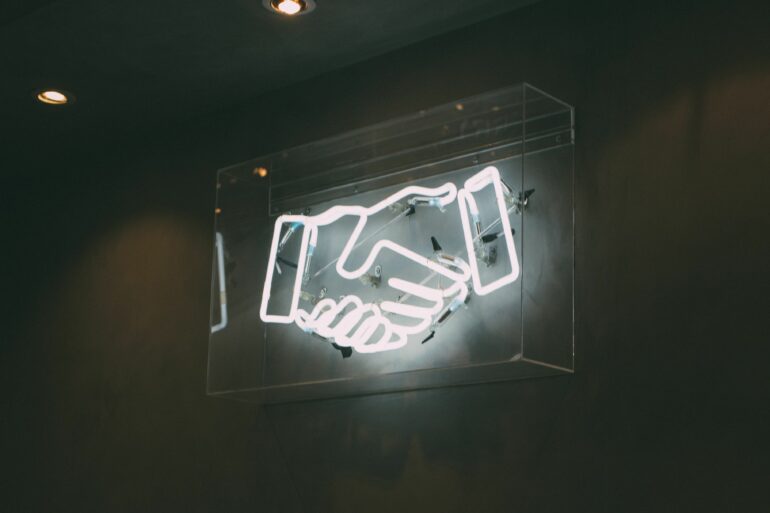 Photo of hand-shake neon lights flashing on the wall at night