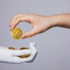 Photo of a human hand giving a crypto coin to a robotic hand, symbolising centralised finance working with decentralised finance