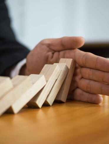 Photo of a hand stopping dominoes from falling in mid-action. A great example of risk orchestration and management.