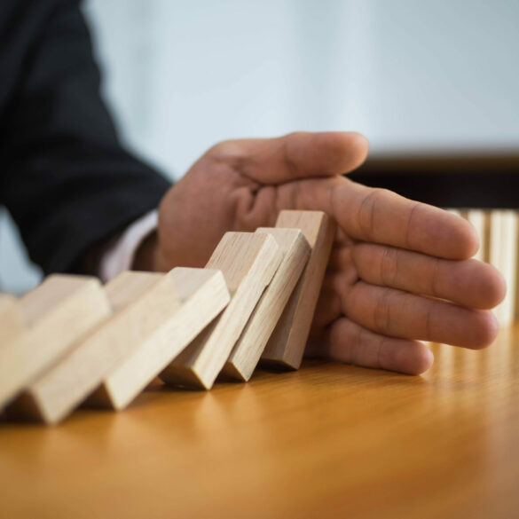 Photo of a hand stopping dominoes from falling in mid-action. A great example of risk orchestration and management.