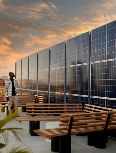 The terrace of a corporate building with solar panels on top designed in a modern fashion as three people walk around and point at them.