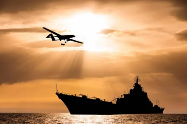 Photo of an armed drone with a big ship in the background during sunset in the sea