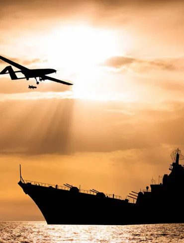 Photo of an armed drone with a big ship in the background during sunset in the sea