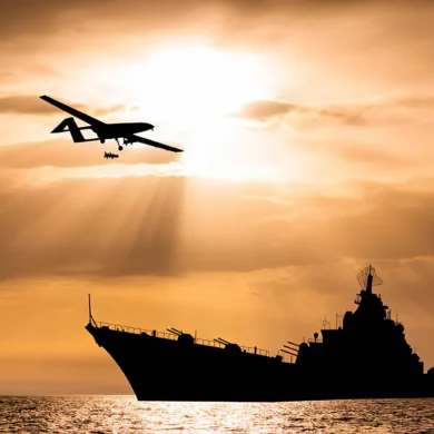 Photo of an armed drone with a big ship in the background during sunset in the sea