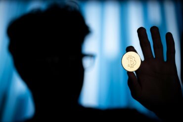 Photo of a shadowed man holding a Bitcoin coin