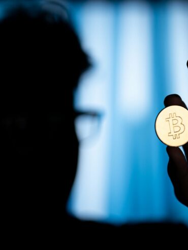 Photo of a shadowed man holding a Bitcoin coin