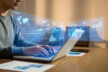 Man looking at his laptop on his desk with blue-coloured financial graphics overlayed on the screen, depicting a fintech executive at work.